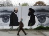FILE PHOTO: An Afghan man wearing a protective face mask walks past a wall painted with photo of Zalmay Khalilzad, U.S. envoy for peace in Afghanistan, and Mullah Abdul Ghani Baradar, the leader of the Taliban delegation, in Kabul