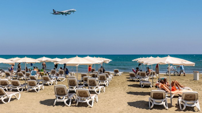 Reiserecht: Touristen am Strand von Larnaca, Zypern, beobachten die Landung eines Passagierflugzeugs