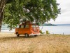 Ein Campingbus Volkswagen VW Bulli T2 steht unter Bäumen in der Landschaft an einem Seeufer, Bolsena, Latium, Italien. M; Camping