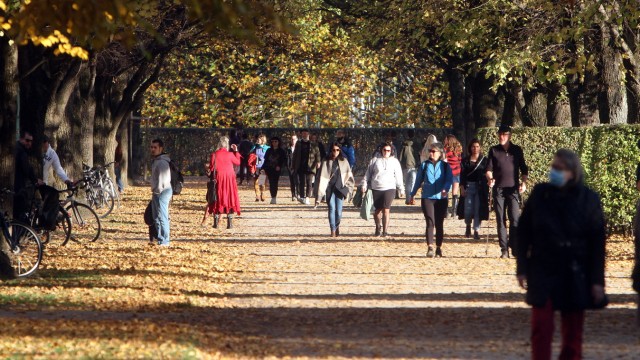 Passanten genießen den warmen und sonnigen Herbsttag bei einem Spaziergang durch den herbstlichen bunten Hofgarten der