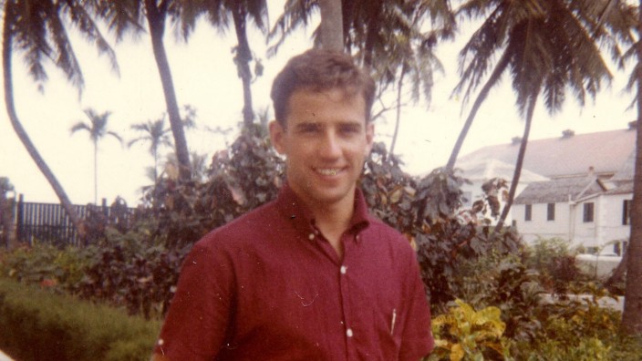 Joe Biden als Student in einem kurzärmeligen roten Hemd vor Palmen in einem Park.