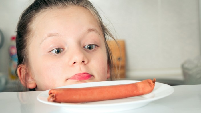 Cute Girl Looking At Sausage In Plate While Peeking Over Table