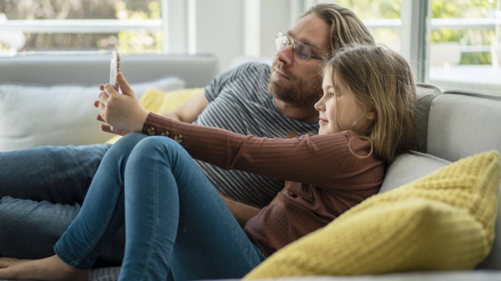 daughter taking selfie through phone with father on sofa model released Symbolfoto property released JOSEF01565