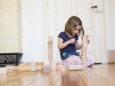 Little girl crouching on floor playing with wooden building bricks model released Symbolfoto PUBLICA