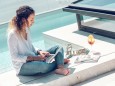 Pretty young female in casual outfit smiling and browsing modern laptop while sitting on poolside on sunny day Copyright