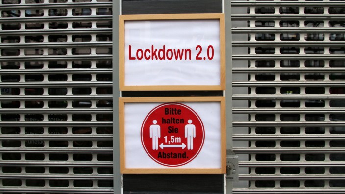 (FOTOMONTAGE) Schild mit Aufschrift Lockdown 2.0 hängt am Eingang eines mit Rolltor verschlossenen Geschäfts in der Inn