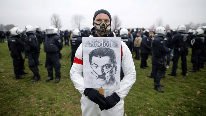 Ein Demonstrant posiert mit einem im Stile Adolf Hitler verfremdeten Konterfei von Markus Söder, betitelt als Södolf ,