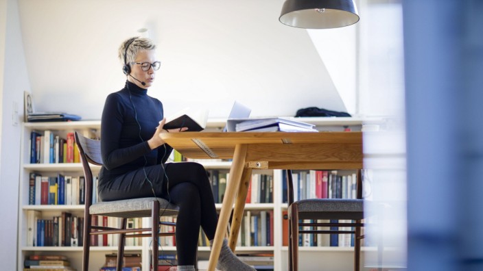 Symbolfoto zum Thema Homeoffice. Eine Frau sitzt zu Hause am Schreibtisch. Sie traegt ein Headset und nimmt an einer Vid