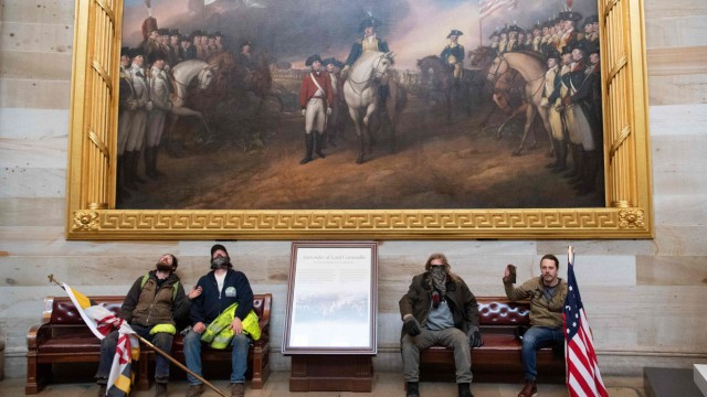 Das Politische Buch: 6. Januar 2021: Anhänger des abgewählten Präsidenten Donald Trump ruhen sich nach dem Sturm aufs Kapitol aus - unter einem Gemälde aus der Frühzeit der USA. Es zeigt die endgültige Kapitulation der Briten nach der Schlacht von Yorktown im Jahr 1781.