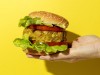 Cropped unrecognizable person hand holding a homemade vegan green lentil burger with tomato, lettuce and french fries on