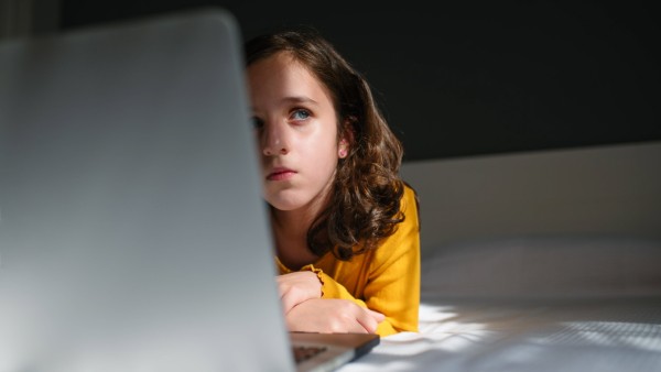 Pensive preteen girl looking away while lying down in bed with a laptop computer Copyright: xIsraelxSebastianx