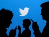 FILE PHOTO: Smartphone users are silhouetted against a backdrop projected with the Twitter logo