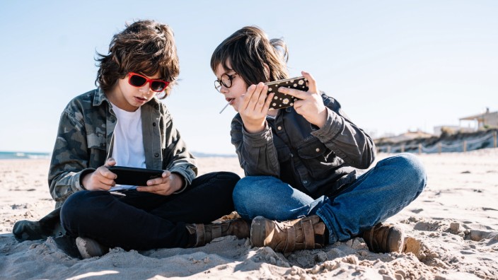 Two children playing with their mobile on the beach on a sunny winter day Copyright: xMikelxPoncex