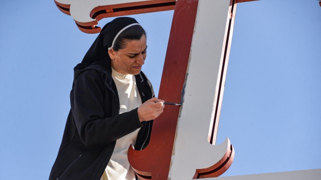Eine Nonne in Karakosch hübscht ein Kreuz mit etwas Farbe auf.