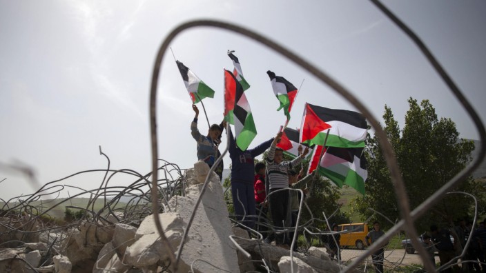 Nahost: Frieden in Gefahr: Palästinensische Jugendliche demonstrieren mit Flaggen vor einem im Konflikt demolierten Haus.