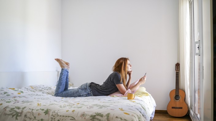 Young woman at home chilling in bedroom and using her smartphone