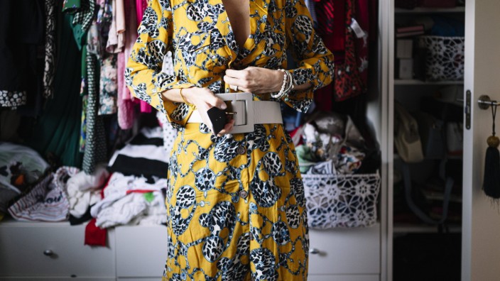 Mid adult woman fastening belt on new yellow dress in wardrobe at home model released Symbolfoto property released JCMF0