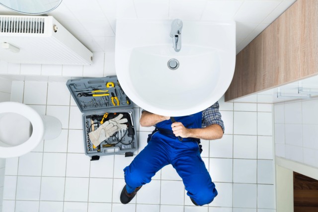 High Angle View Of Male Plumber Repairing A Sink In Bathroom model released Symbolfoto PUBLICATIONxI