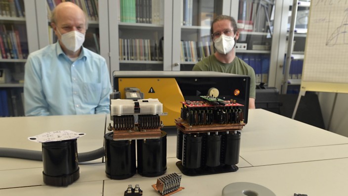 von links:  Prof. Thomas Weyh, Manuel Kuder; 
hinten: herkömmliches Gerät zu Magnetstimulation, vorne ((schwarze Teile mit Aufbau)) neu entwickelte Module (ganz links das neueste)