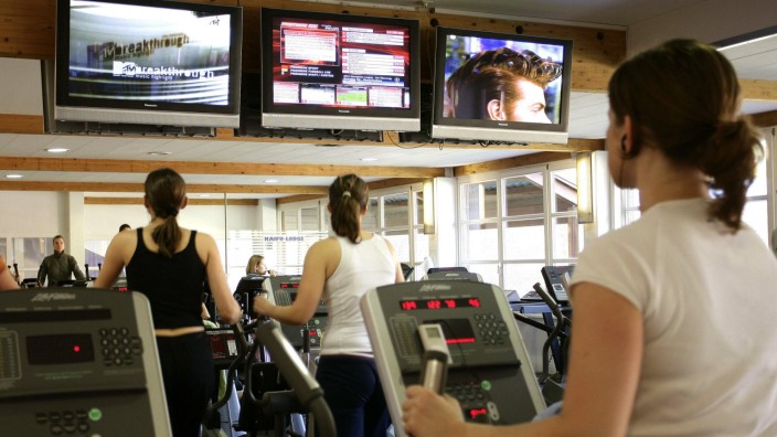 Beschwerde bei Bundesländern: Gäste eines Fitnessstudios trainieren vor Fernsehbildschirmen. Lizenzgebühren sollen ARD und ZDF dafür nicht nehmen.