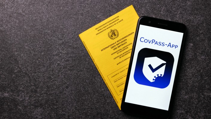 Das Logo der CovPass-App auf einem Handybildschirm neben einem traditionellen Impfbuch. Der Schriftzug CovPass-App wurde