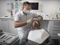 Thema: Zahnarzt mit Lupenbrille setzt eine Spritze zur Lokalanaesthesie. Bonn Deutschland *** Topic Dentist with magnify