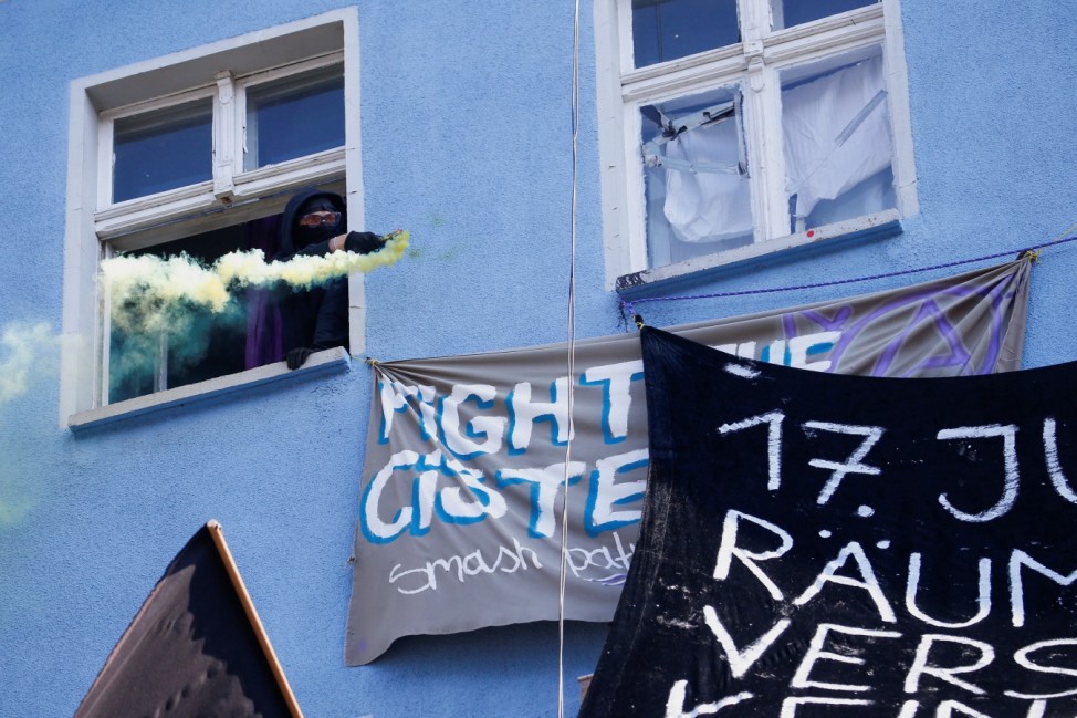 An activist holds a smoke flare out from a window at a Rigaer street building in Berlin