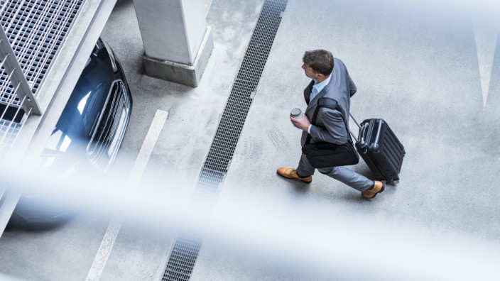 Top view of businessman walking with baggage and takeaway coffee at a car park