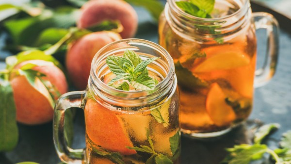 Summer refreshing cold peach ice tea with fresh mint in glass jars on metal tray over rustic wooden garden table, selective focus, copy space (sonyakamoz)