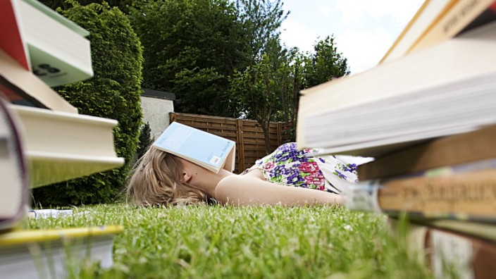young woman lying on grass in garden reading books