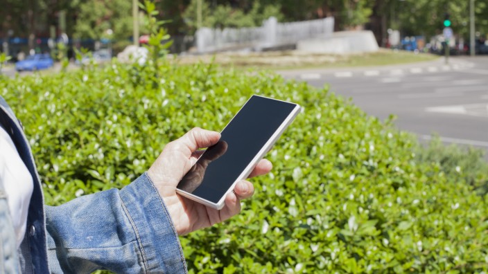 hand of woman blue jeans jacket with mobile phone smartphone blank screen in her hands green bush in urban street (quintanilla)