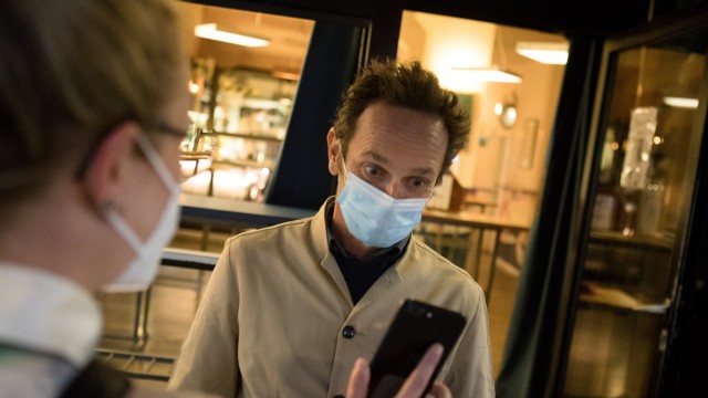 Fünf für München: Ein Gast zeigt Florian Schönhofer im Café Kosmos seinen Impfnachweis am Smartphone. Er hat vergangenes Jahr eine Impfaktion gestartet.