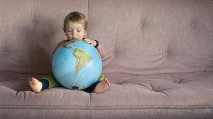 Typisch deutsch: Ein Kind sitzt auf dem Sofa und untersucht einen Globus.
