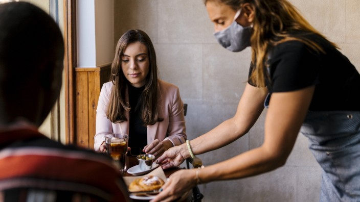 Covid Disease: A waitress serves two guests.  Due to the lack of skilled workers, catering staff are particularly affected when colleagues report for illness.