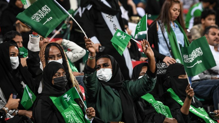 Saudi Arabian football fans hold up their national flags to show support for Saudi Arabia national f; Saudi Arabian women cheer after Saudi Arabia routed North Korea 4-0 in Asian Cup