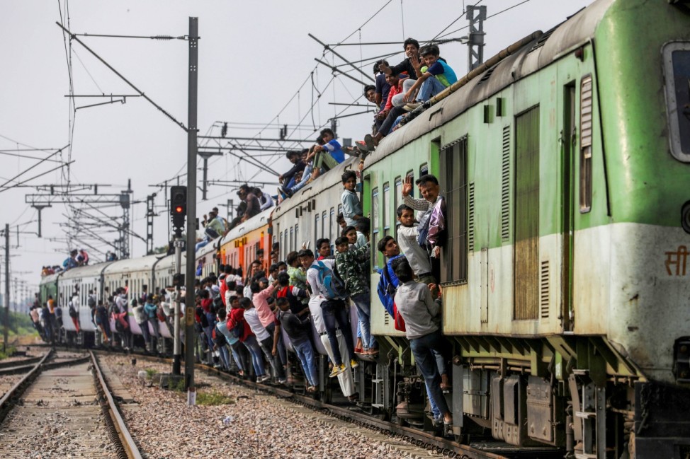 People cling on to a crowded train as it leaves a railway station during the ongoing Coronavirus Disease (COVID-19) outbreak in Ghaziabad