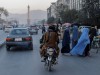 A group of women wearing burqas crosses the street as members of the Taliban drive past
