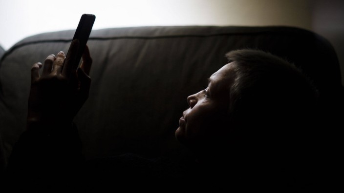 Eine Frau sitzt nachts auf der Couch und schaut in ein Smartphone