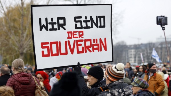 Ein Demo-Teilnehmer aus dem Umfeld der Corona Rebellen Düsseldorf bahnt sich mit einem Schild den Weg durch Demonstrant