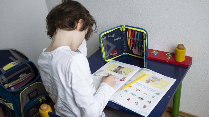 Erstklaessler (7. Jahre) sitzt an einem Tisch zu Hause und macht Deutsch Aufgaben in seinem Heft Buchstabenheft - Grunds