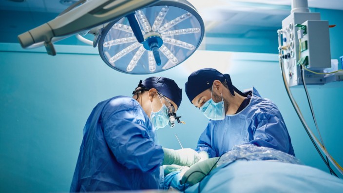 Side view of unrecognizable male doctor with assistant in medical gowns and masks performing surgery with laser in opera