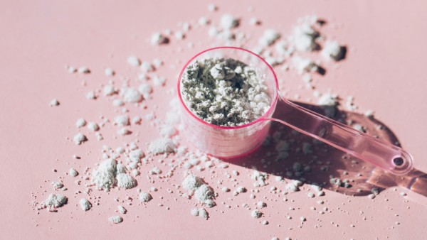 Measuring spoon with collagen powder or alginate mask on pink background