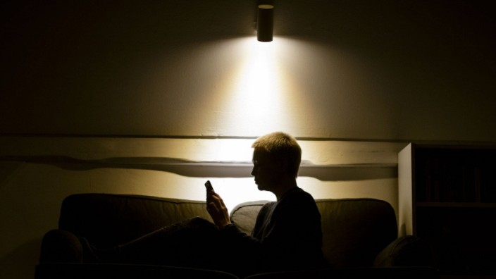 Symbolfoto zum Thema Einsamkeit und Isolation: Eine Frau sitzt nachts auf der Couch und schaut in ein Smartphone. Berlin