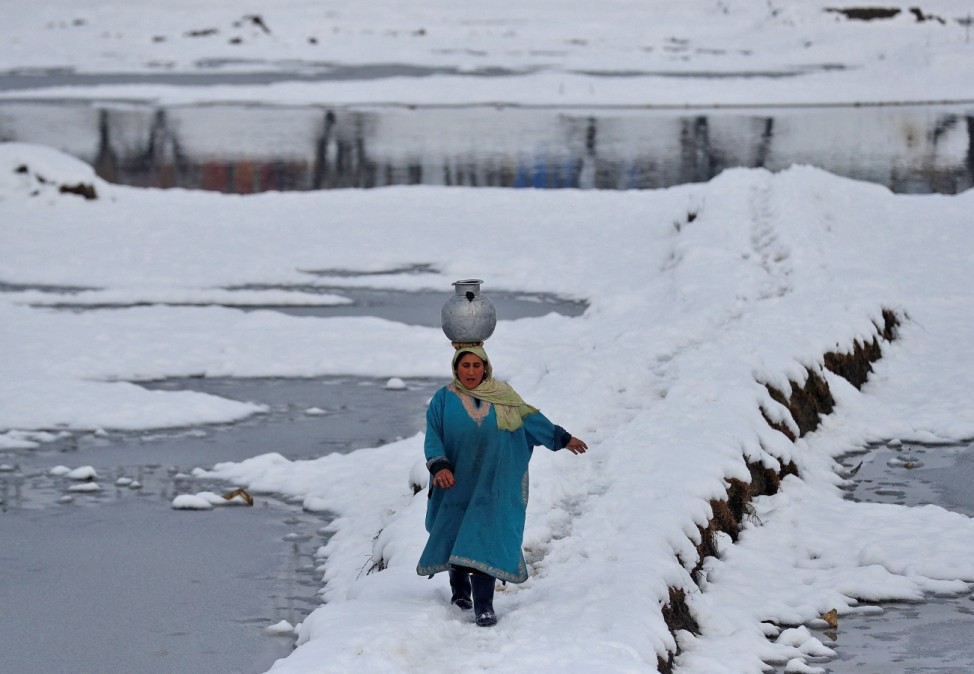 Woman carrying a water pitcher walks through a snow-covered field on outskirts of Srinagar