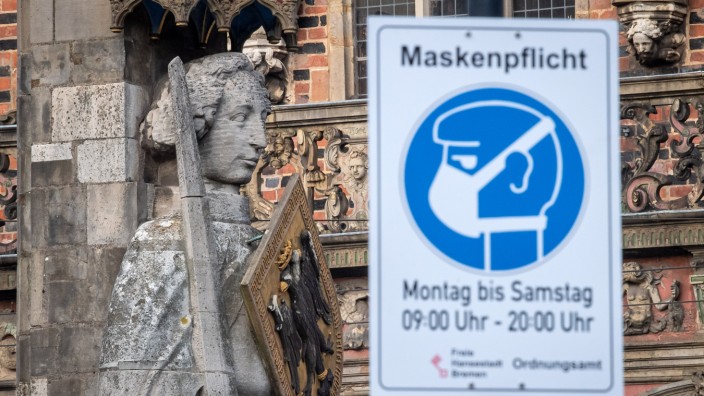 Bremen: Der deutsche Impfmeister unter den Städten als Corona-Hotspot: Vor dem Bremer Roland, einem Wahrzeichen der Stadt, weist ein Schild auf die Maskenpflicht hin.