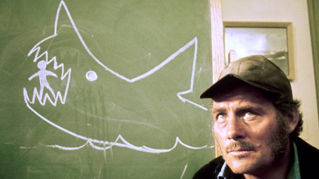 Mode und Popkultur in den USA: Die Kappe als Erkennungszeichen der einfachen Leute: Robert Shaw als Haifischjäger Quint im Thriller "Der weiße Hai".