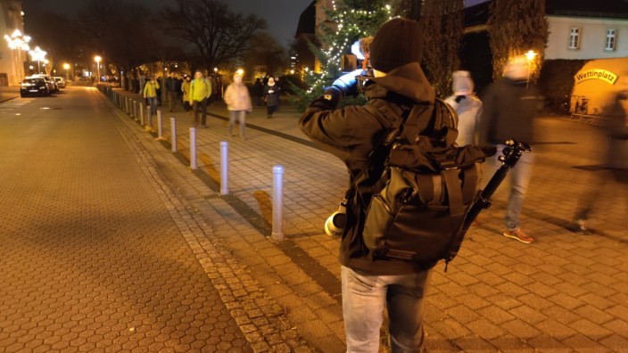 Pressefreiheit: Coswig in Sachsen. Der Journalist läuft los, fotografiert, mit Blitz in der Dunkelheit. Die Protestierenden starren den Reporter an und fragen, für wen er arbeite.
