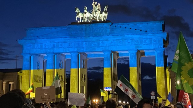 Syrer in Deutschland: Während einer Solidaritätsdemo wird das Brandenburger Tor in den Nationalfarben der Ukraine angestrahlt. Über den Köpfen der Demonstranten ist auch die alte syrische Flagge zu sehen, die von der syrischen Opposition wieder benutzt wird.