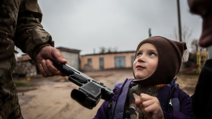 Fotografie: Ein Soldat hält einem kleinen Jungen eine Waffe hin, damit der frühzeitig lernt, damit umzugehen. Die Aufnahme von David Tesinsky ist 2017 in der Nähe von Luhansk entstanden.