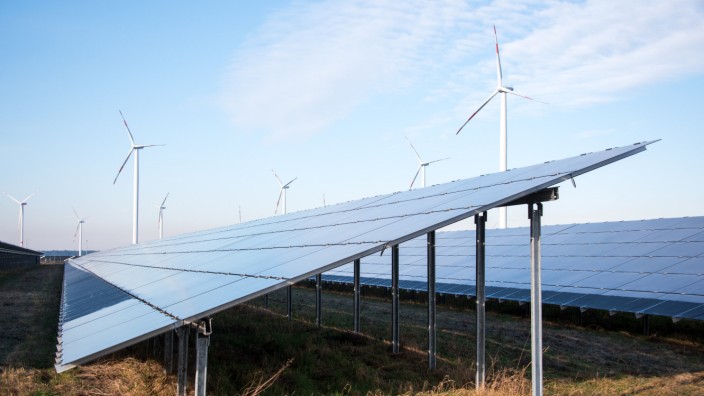 Energiekrise: Blick auf einen Solarpark, im Hintergrund sind Windräder zu sehen.